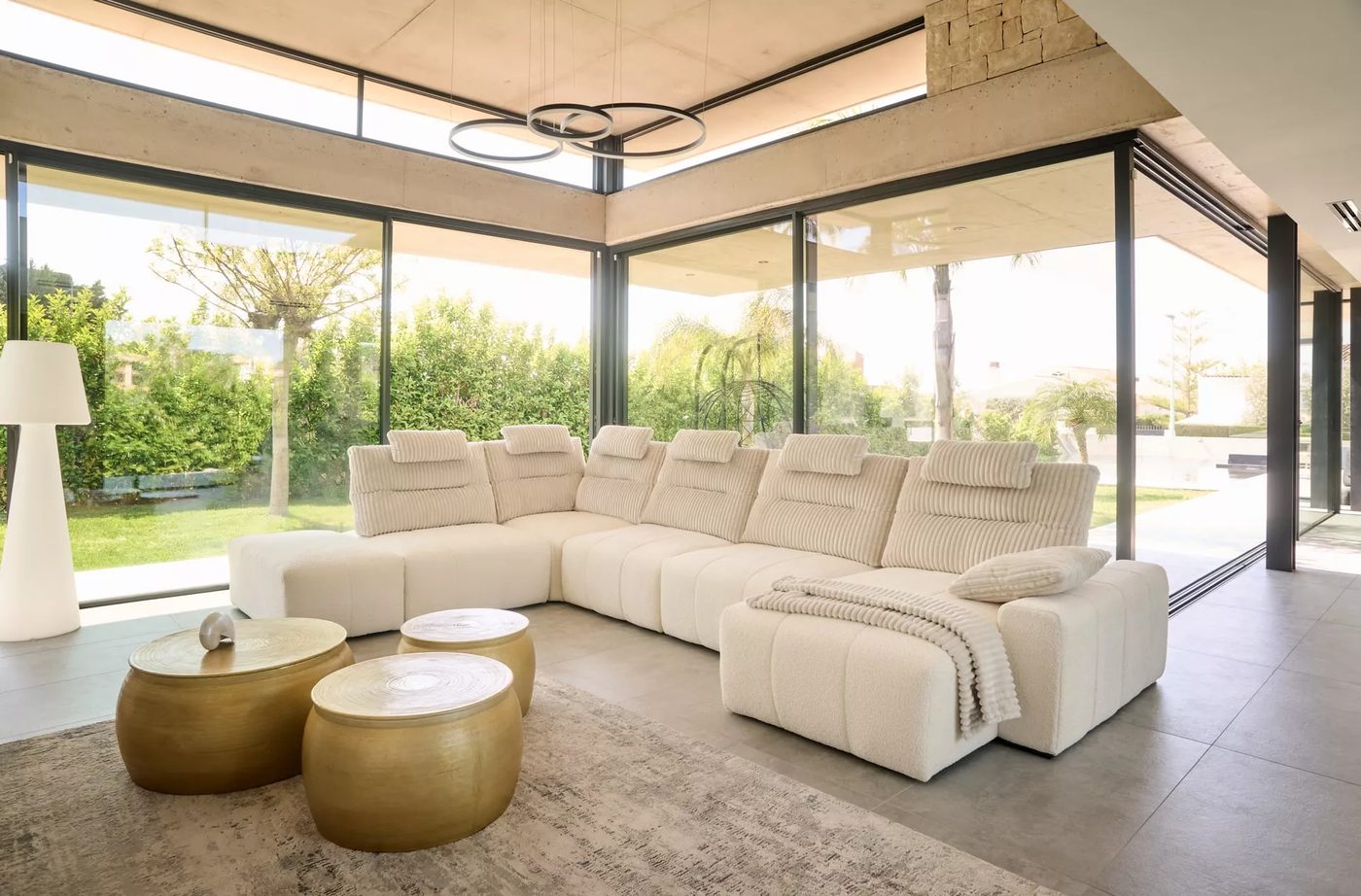 Grand canapé d'angle Acomodel crème dans un salon vitré ouvert sur le jardin